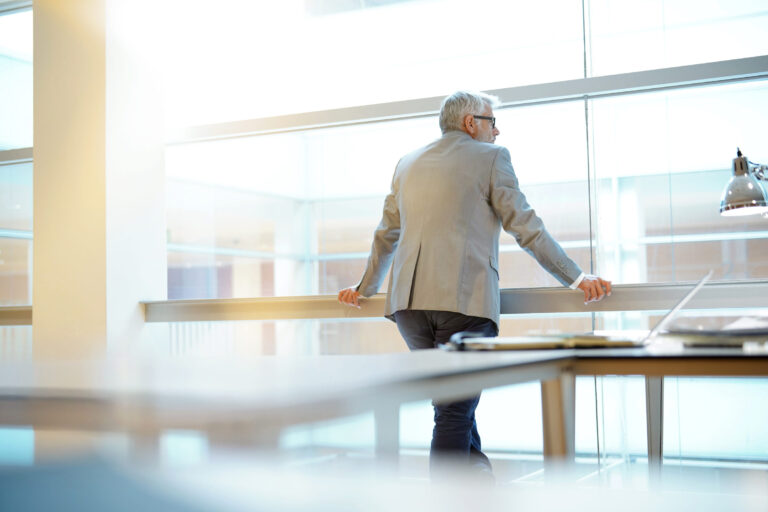 Middle-aged man in suit and glasses standing by the window in the AvreaFoster conference room looking out at the city.