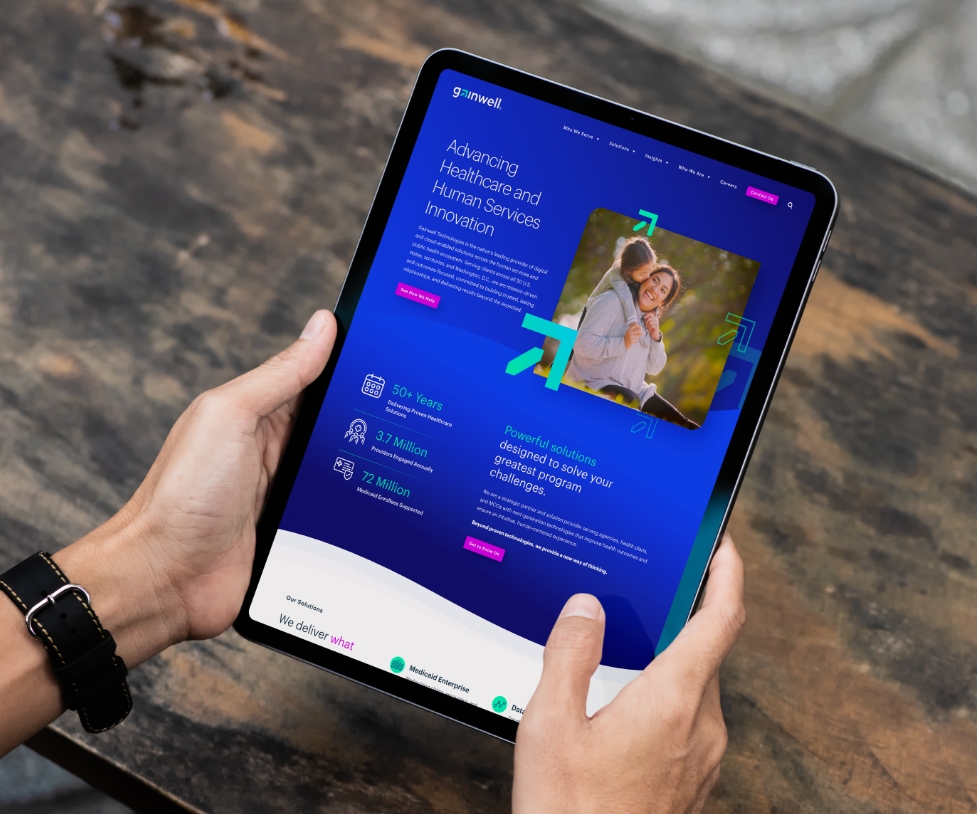 Tablet in the hands of a person with a black watch showcasing a page from the Gainwell Technologies website